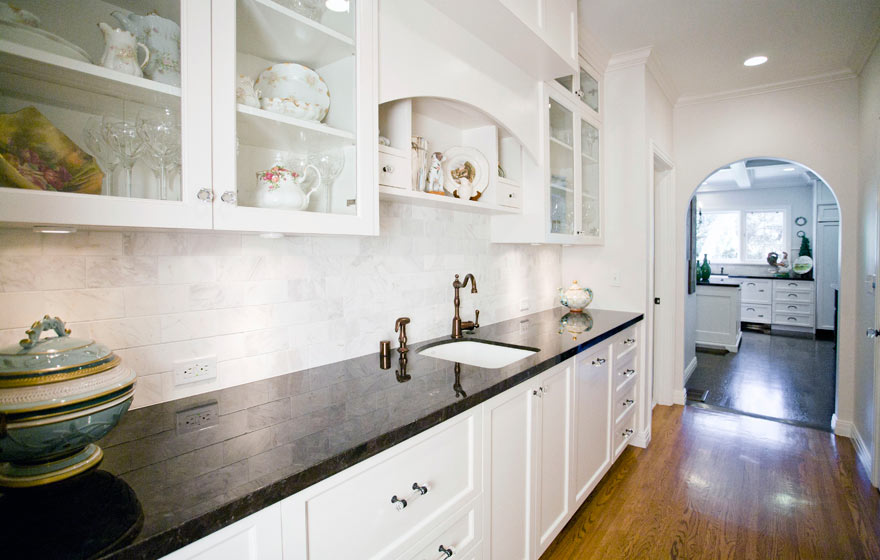 Glass upper cabinets allow cabinetry to extend to the ceiling and add ample storage to this open space.